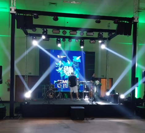 Locação de Equipamentos, estrutura de palco com luzes, montagem segura em ambiente interno, iluminação frontal para artista, pontos de fixação truss, posicionamento de refletores, suporte para moving heads, organização de cabos e energia, palco para cerimônia e festa, cenário iluminado para banda, layout de apresentação no salão, instalação com alinhamento, suporte técnico na montagem, iluminação de destaque no palco, truss com travamento firme, palco bem iluminado, aluguel de estrutura para eventos